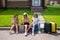 Three Caucasian women and a dog go on a trip. The girls are sitting on the curb with suitcases and waiting for a taxi