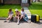 Three Caucasian women and a dog go on a trip. The girls are sitting on the curb with suitcases and waiting for a taxi