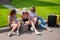 Three Caucasian women and a dog go on a trip. The girls are sitting on the curb with suitcases and waiting for a taxi