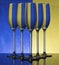 Three champagne glasses on a shiny surface with water that distort yellow and blue background