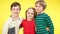 Three charming children hugging at yellow background and smiling looking at camera. Portrait of friends or siblings