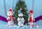 Three cheerful snowmen are standing under a christmas tree on a blue background