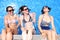 Three cheerful young women simulate that they sit over a pools edge with a water wall backwards