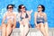 Three cheerful young women simulate that they sit over a pools edge with a water wall backwards