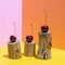 Three cherries on small wooden stumps eaten by bark beetle on bright pink, yellow and orange backdrop.