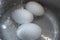 Three chicken eggs in boiling water in metal kitchen pot