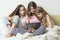 Three children girls sitting at home in bed looking at a digital tablet with interest and emotions