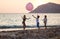 Three children playing with huge pink balloon on beach at sunset