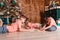 Three children sit on the floor near the Christmas tree and draw