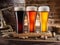 Three chilled glasses of different beer and beer barrel on wooden table closeup