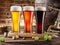 Three chilled glasses of different beer and beer barrel on wooden table closeup