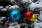 three Christmas tree decorations blue, red and yellow hang on a spruce branch sprinkled with snow, and against the background of a