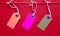 Three colored bright tags hang on a red rope on a red background. Copy space, place for text, flat lay