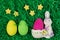 Three colored easter eggs, decorative bunny bowl and stars in green grass.