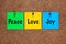 Three colored notes on corkboard with words Peace, Love, Joy