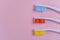Three colored toothbrushes on a pink background. Red, yellow, blue