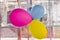 Three colorful balloons, blue, pink and yellow, stuck on a plastic window.