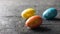 Three colorful eggs on a dark wooden table. The decoration of the Easter table.