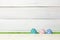 Three colorful handmade easter eggs stand on a green lawn, covered with a barrier, on a white wooden background with space on the