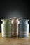 Three colourful ceramic canisters on timber bench with grey spot on background