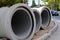 Three concrete pipes lie on the unfinished sidewalk near the road at the site of the road construction works in the city