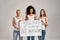 Three confident diverse women in white shirt and casual denim jeans holding, standing with a banner in their hands