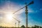 Three construction cranes in a row, against sunlight with beautiful blue sky.