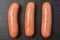 Three cooked sausages on a black basalt background