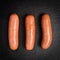 Three cooked sausages on a black basalt background