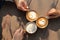 Three cup of different coffee which are cappuccino, mocha and caramel milk holding by hand of friend on the wooden rustic table in