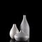 Three curvy white vases on black, with reflection.