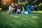 Three cute girls relax and socialize on the lawn in the summer park. Young women on the green grass among the trees, looking