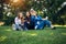 Three cute girls relax and socialize on the lawn in summer park. Young women sit on the green grass among the trees and look