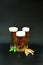 Three different glasses of light beer and foam stand on a black background, next to hops and ears of barley