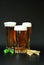 Three different glasses with light beer and froth on top, barley ears and hops next to them on a black background