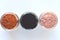 Three different mineral clays for facial masks - pink clay, red clay and activated charcoal in glass jars top view on white