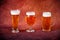 Three differently shaped glasses with light beer stand in a row on a brown background. Close up shot