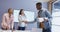 Three diverse male and female architects standing at table shaking hands in meeting room