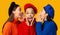 Three Diverse Millennial Girls Gossiping Standing On Yellow Background, Panorama