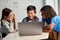 Three diverse schoolmates watching video together on laptop in classroom.