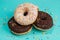 Three donuts, one on top of another, chocolate and white cream on turquoise wooden background