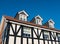 Three dormer windows in the roof of a Tudor style black and white English residential home against a blue sky.