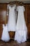 three dresses are hanging on brown wardrobe, a dress of the bride and her bridesmaids before the wedding, white wedding dresses