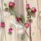 Three dried pink roses, scattered flower petals, green leaves, glass vase on wooden background top view close up