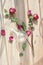 Three dried red roses, scattered flower petals, green leaves, glass vase on wooden background top view close up