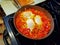 Three egg shakshuka cooking in an iron skillet on a stovetop