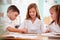 Three Elementary School Pupils Wearing Uniform Using Digital Tablet At Desk