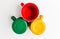 Three enameled cups in green, red and yellow colors on a white background.