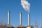 Three factory chimneys against a clear sky. White smoke coming from one of the pipes