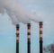 Three factory chimneys release clouds of smoke into the sky.